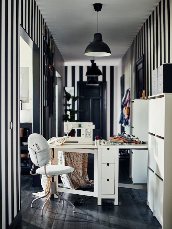 Norden bord utsått i begge ender på et hobbyrom med symaskin, stripete vegger og sort gulv。