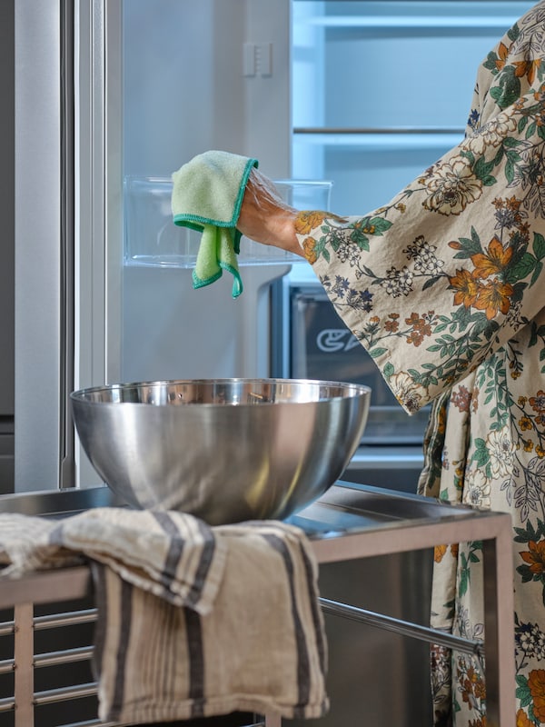 一个人擦拭冰箱内部有绿色RINNIG抹布,加上一个碗和一个茶巾在厨房手推车。