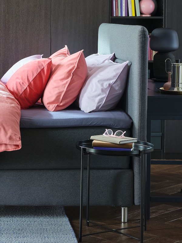 灰色FINNSNES沙发床和床单包括光brown-red ANGSLILJA枕套旁边GLADOM托盘表。