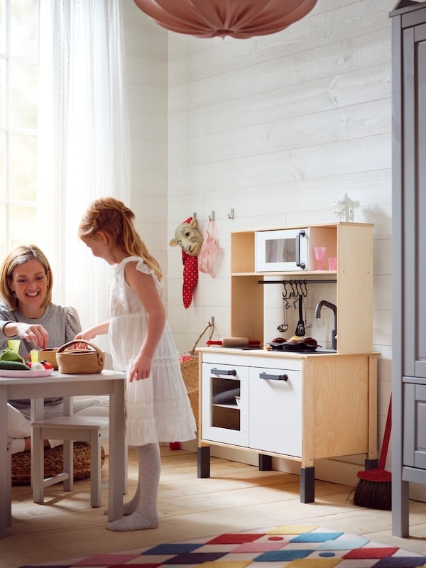 一个女人和一个小孩一起玩SUNDVIK儿童桌子附近的儿童房间DUKTIG厨房玩。