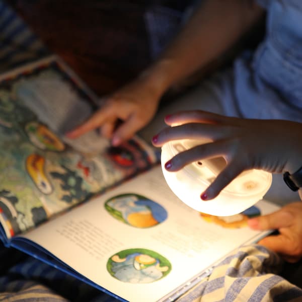 一只手拿着SAMMANLANKAD LED太阳能台灯的光源在页的图画书。