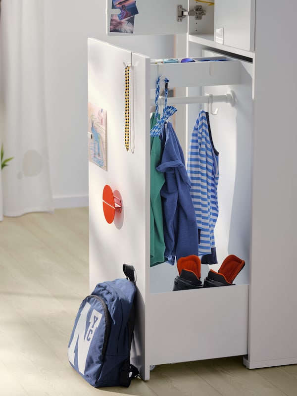 白色SMASTAD衣柜与撤出单位在孩子的房间里挂着衣服上的铁路和一袋斜靠在上面。