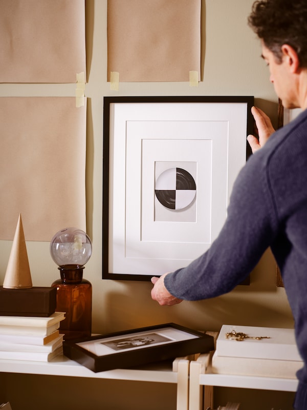 一个人挂一幅画在一个黑色RIBBA框架与牛皮纸米色墙模板贴。