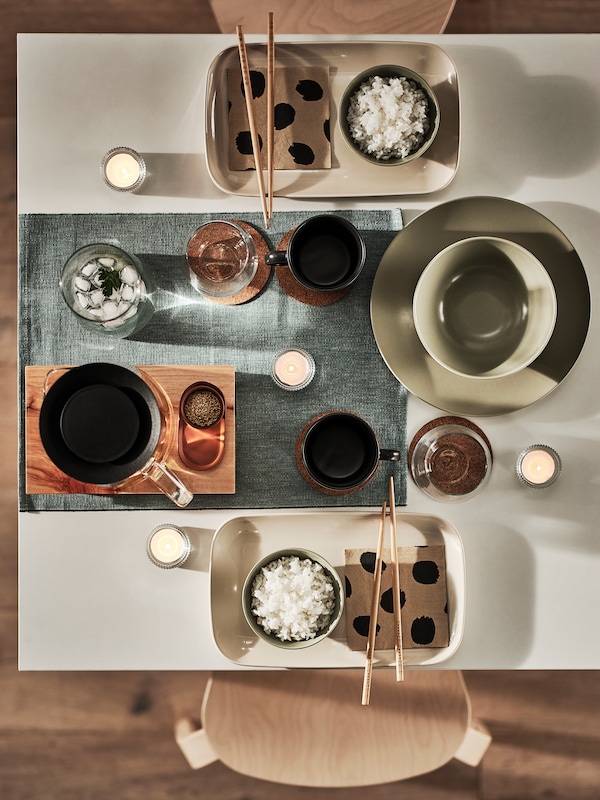 马特绿色FARGKLAR碗和盘子,光滑的米色盘子,深灰色的杯子和一个蓝绿色的地方垫白色桌面。