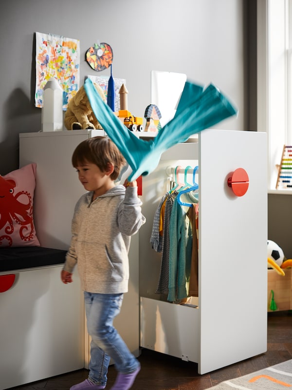 孩子挥舞着蓝色的毛衣在肩膀上,面前的白色SMASTAD衣柜以开放的撤军。