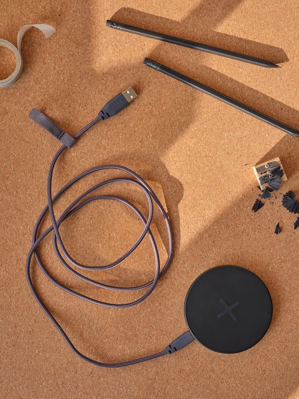 一个深灰色LILLHULT USB-A-to-USB-C绳连接到一个黑色LIVBOJ无线充电器,都放在桌子SUSIG软木垫。