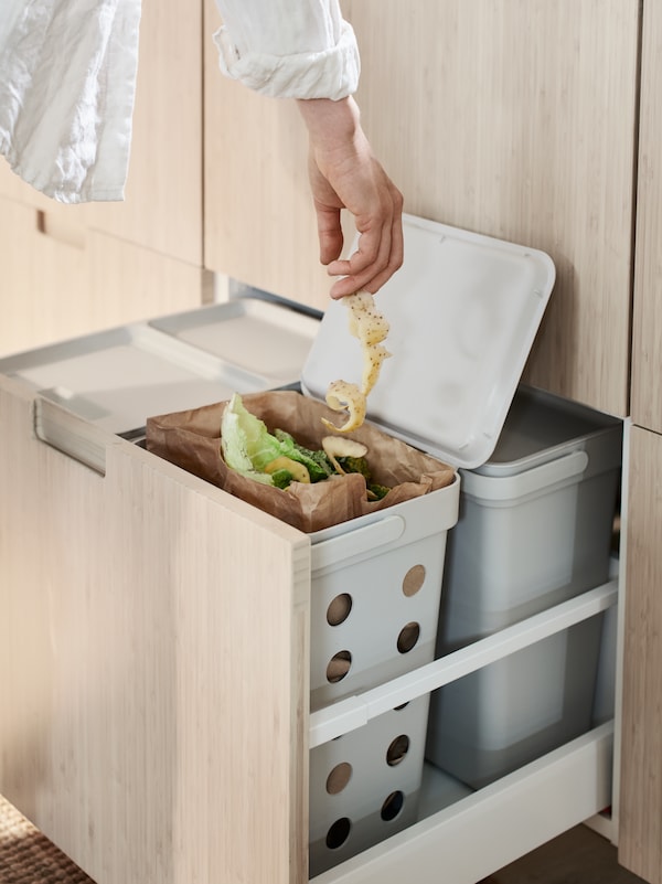 一个人的手将一长串土豆皮放入一个HÅLLBAR的垃圾桶，里面装着有机厨房垃圾。