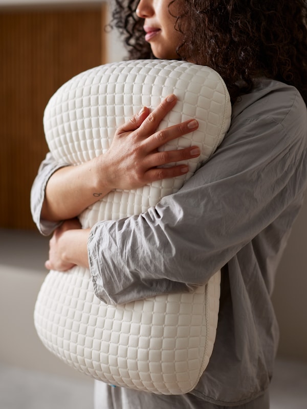 灰色睡衣站在明亮的房间里一个女人拿着KLUBBSPORRE工效学多档位枕头抱在怀里。