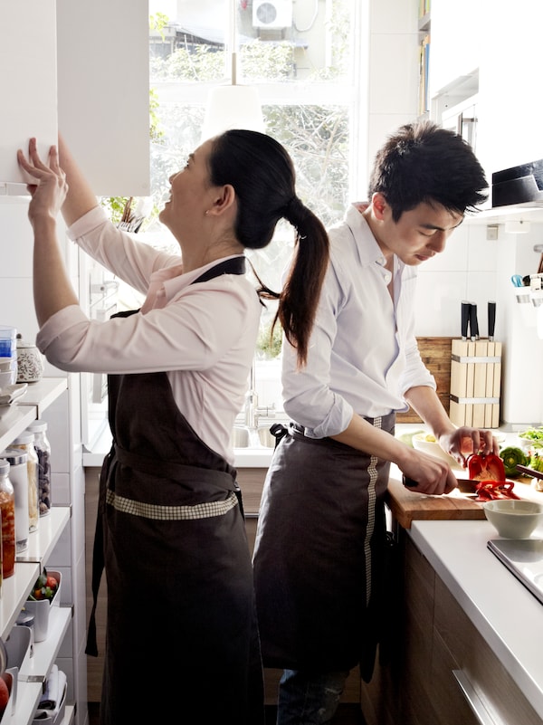 一对年轻的夫妇在他们的厨房厨房准备食物。其中一个排骨胡椒,而另一个看起来在一个壁橱。