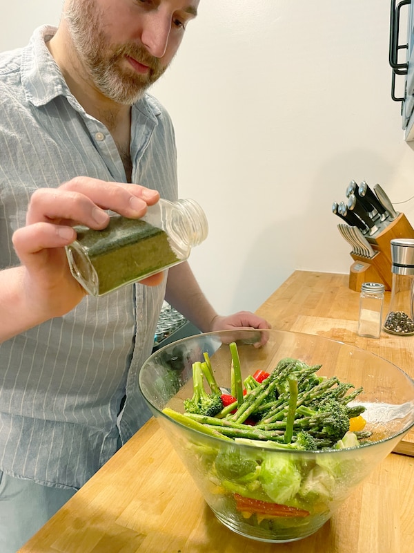 Mężczyzna w kuchni sypie丹尼斯·皮帕兹泽szklanej butelki做miski z gotowanymi warzywami。