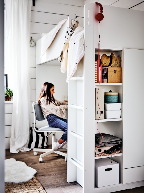 一个年轻的女子坐在一个ORFJALL椅子在书桌下SMASTAD阁楼床。箱存储在货架上在床上框架。