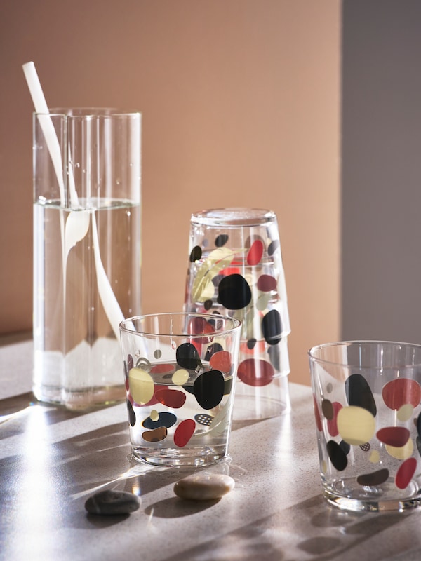 SOMMARFLOX眼镜多色图案的石头和VARMBLIXT玻璃水瓶在透明玻璃站在桌子上。