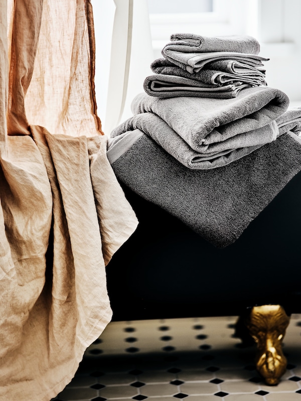 一堆黑色和浅灰色毛巾的黑色roll-top浴用金脚,米色的浴帘。