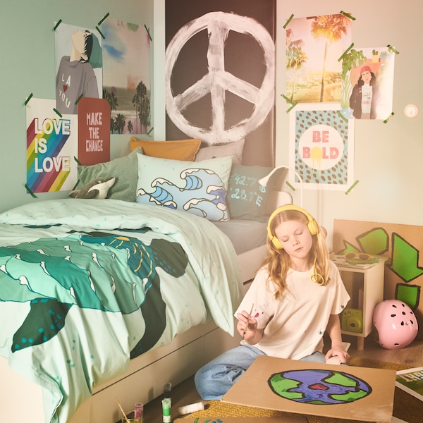 一个女孩,世界的绘画海报,坐在床旁边的地板上穿着BLAVINGAD海龟被套。