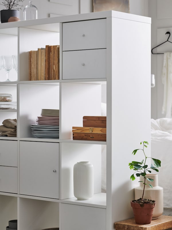 room-dividing白色KALLAX搁置单位持有的一部分书和装饰物品,和门和抽屉插入。