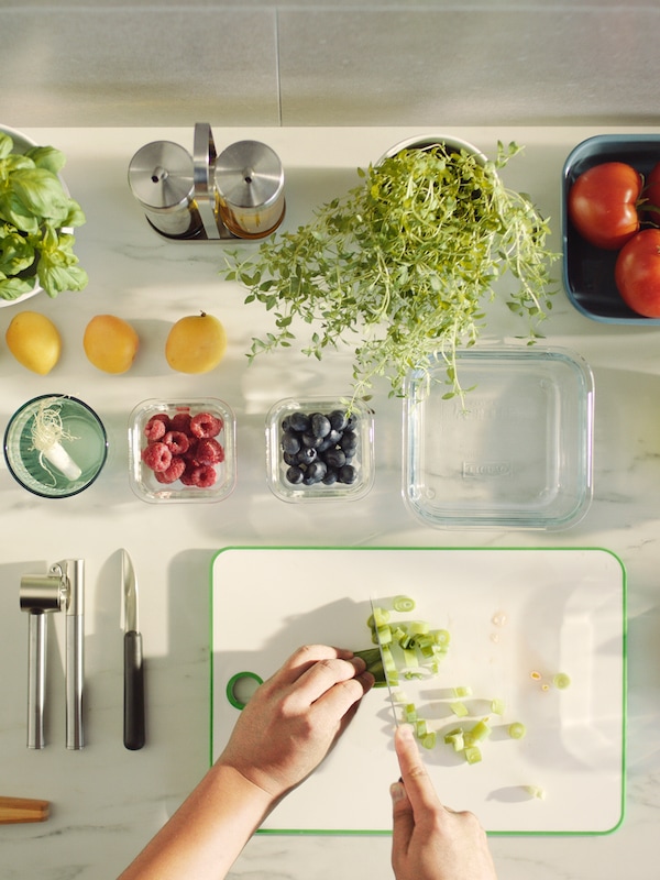 两只手切葱绿色/白色MATLUST案板,旁边的厨房用具和各种水果和香草。