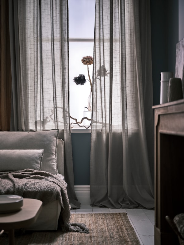 米色SILVERLONN纯粹的窗帘挂在前面的地板上一个窗口旁边自然色彩LOHALS黄麻地毯沙发。