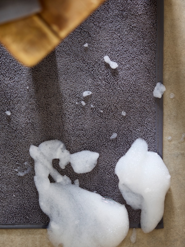 En grå OSBYSJÖN badrumsmatta med fluffigt vitt tvållödder på ett ockrafärgat golv。