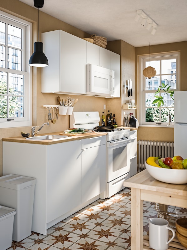 KNOXHULT厨房在白色电车一碗水果,两扇窗户,灰色的垃圾桶和一个深灰色的吊灯。