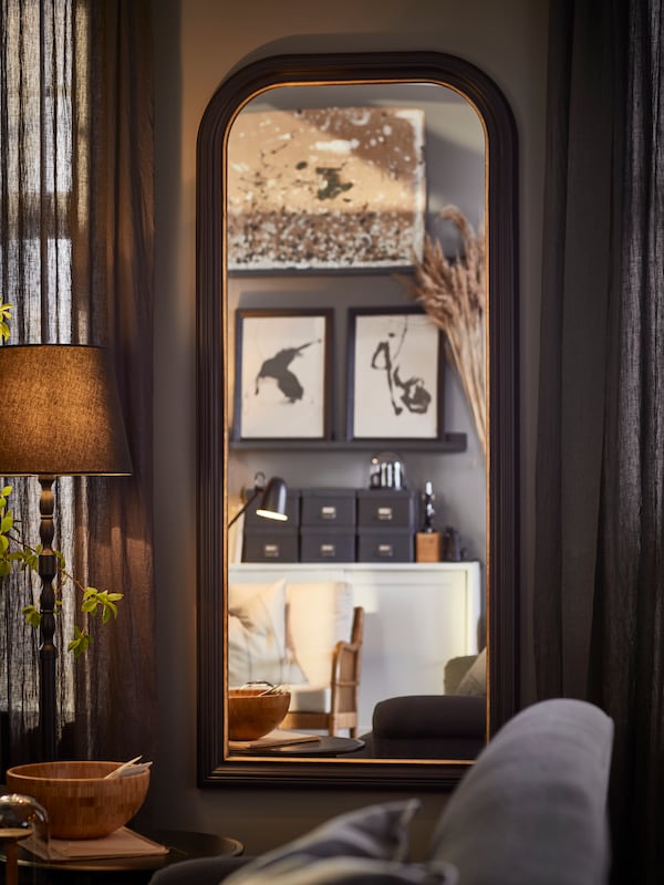 黑色ALMAROD镜子挂在客厅,反映图像的壁板与框架艺术品在对面的墙上。