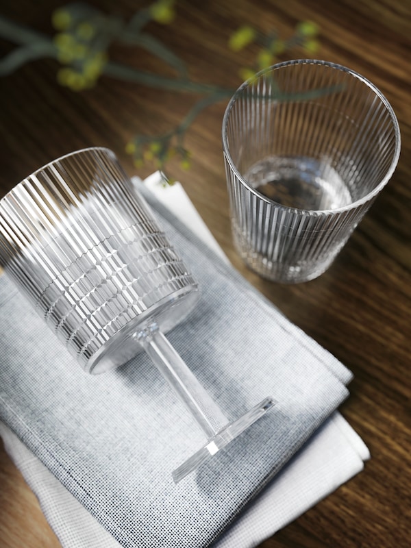 Nahaufnahme进行KALLSINNIG格拉斯来自transparentem Kunststoff neben einem KALLSINNIG Weinglas, das auf静脉餐巾liegt。