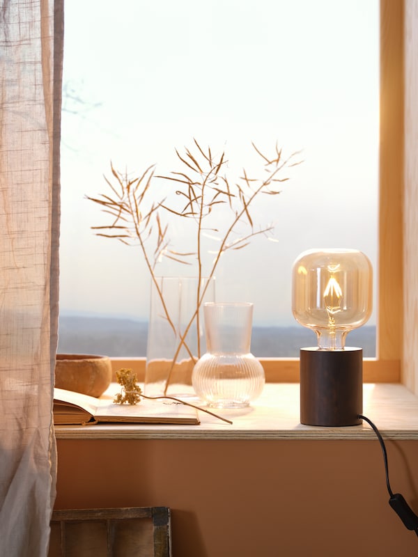 两个透明玻璃花瓶,CHILIFRUKT和PADRAG坐在明亮自然的窗口旁边的一个乡村风格的灯泡