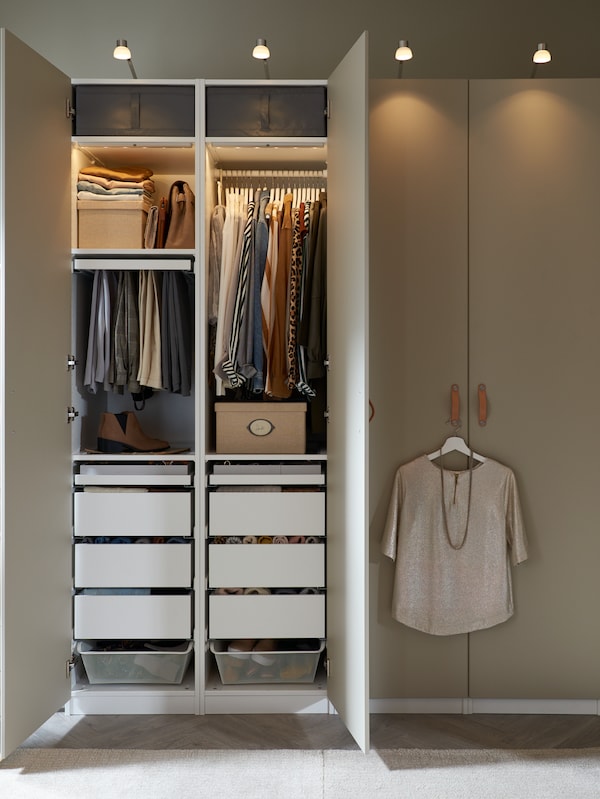 并排PAX衣柜与grey-beige REINSVOLL门。组织一个衣柜打开,露出整齐的衣服里面。