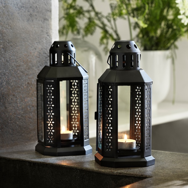 两个ENRUM灯笼光喝茶,每个包含一个点燃茶灯,站在一个黑暗的灰色石头架子上。