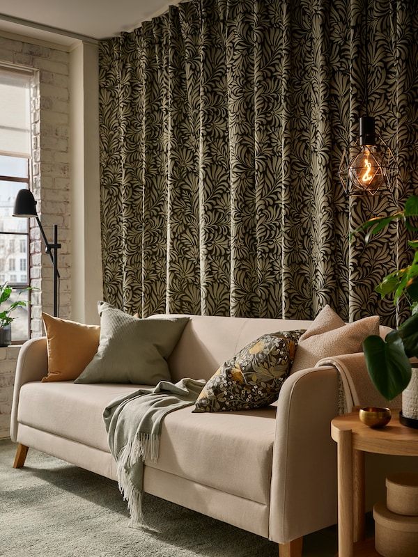 深绿色叶子图案TRAGSPINNARE窗帘挂在墙后面米色沙发与各种靠垫和抛出。