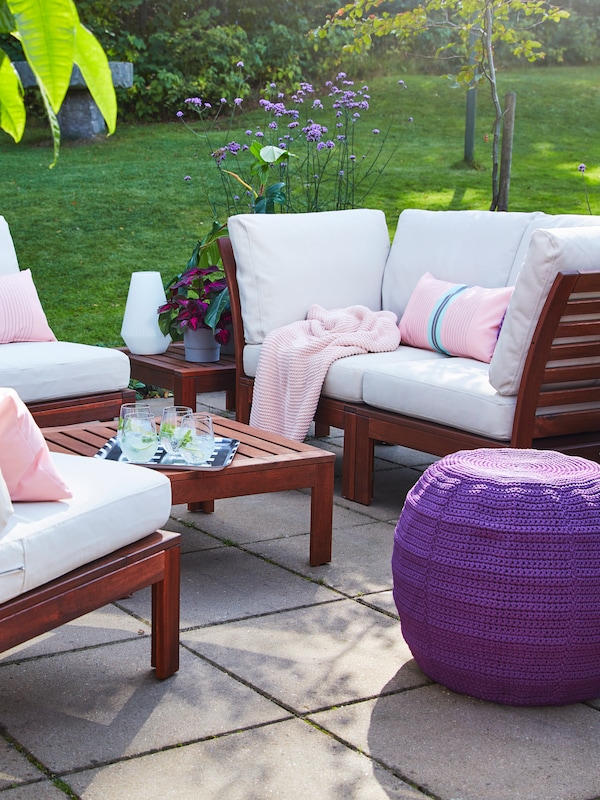 一套阀座的谈话和皂荚木桌子,米色户外垫子,一个紫色的大坐垫和粉红色的垫子。