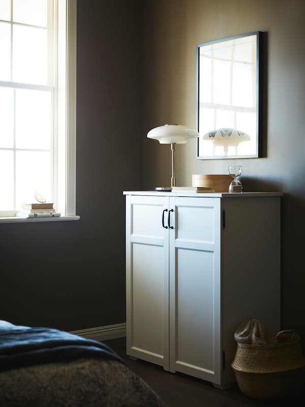 TALLBYN台灯在白色GREAKER柜的抽屉里,由一个大窗户在一个昏暗的房间里。