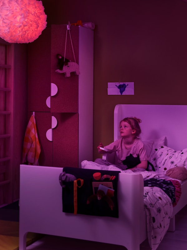 一个女孩使用STYRBAR遥控改变TRADFRI LED灯泡的颜色紫色VINDKAST吊灯。