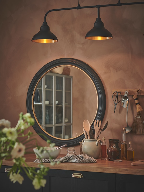 黑色ALMAROD镜子挂在一个apricot-coloured墙一个乡村风格的厨房,厨房工作台上方。
