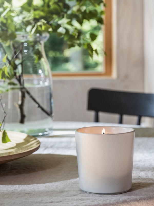 ADLAD带香味的蜡烛在一个陶瓷罐和一个清晰的花瓶的树枝上餐桌靠近窗口。