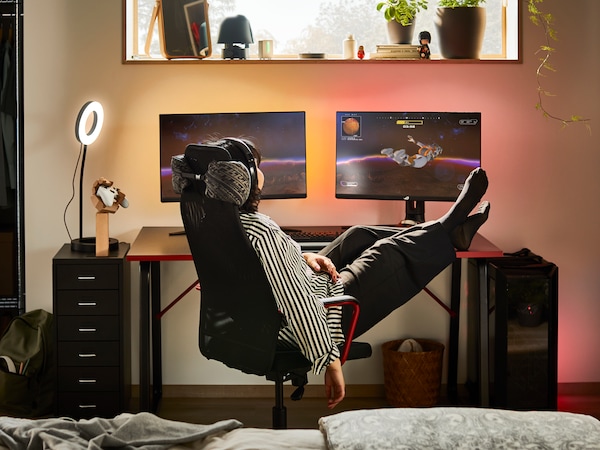一个昏暗的房间,一个人躺在一个黑色HUVUDSPELARE游戏双屏幕黑HUVUDSPELARE桌子椅子。