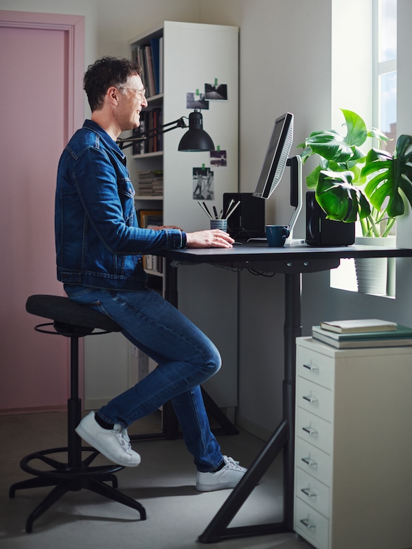 人一个家庭办公室,靠着LIDKULLEN工作时符合人体工程学的凳子上。