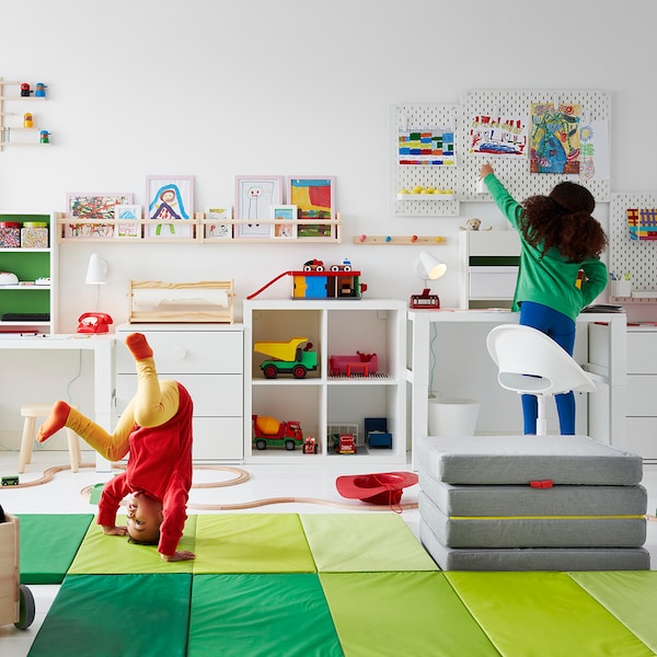 孩子穿着红色和黄色是站在PLUFSIG健身垫在一个游戏室和玩具包围着。