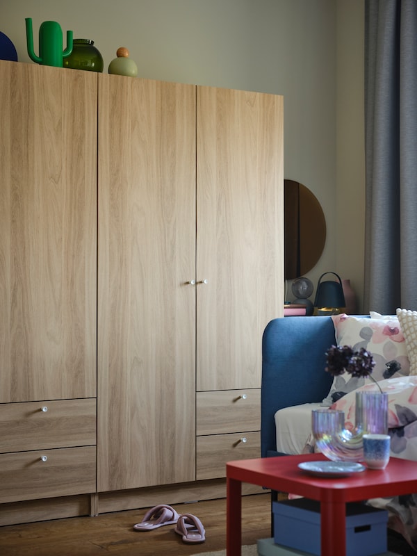 两个oak-effect VILHATTEN衣柜并排在工作室卧室床头板与蓝色BLAKULLEN床角落在前面。