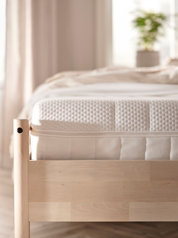 光的木制床框架AKREHAMN泡沫床垫,一个站在窗户前的米色的卧室。
