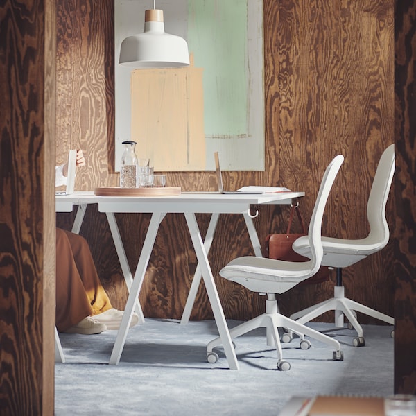 Wyłożona wykładzinądywanowąprzestrzeńkonferencyjna z brązowymi drewnianymi panelami naścianach, dwoma białymi biurkami TROTTEN我dwoma beżowo-białymi krzesłami biurowymi LANGFJALL。