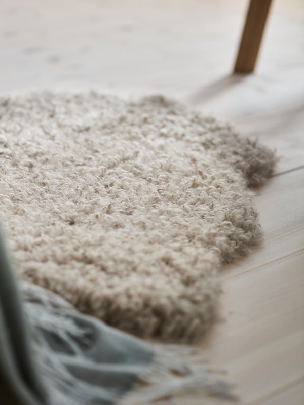 米色SVINDINGE地毯,sheepskin-style地毯,但是是由回收PET瓶,躺在一个木制的地板上。