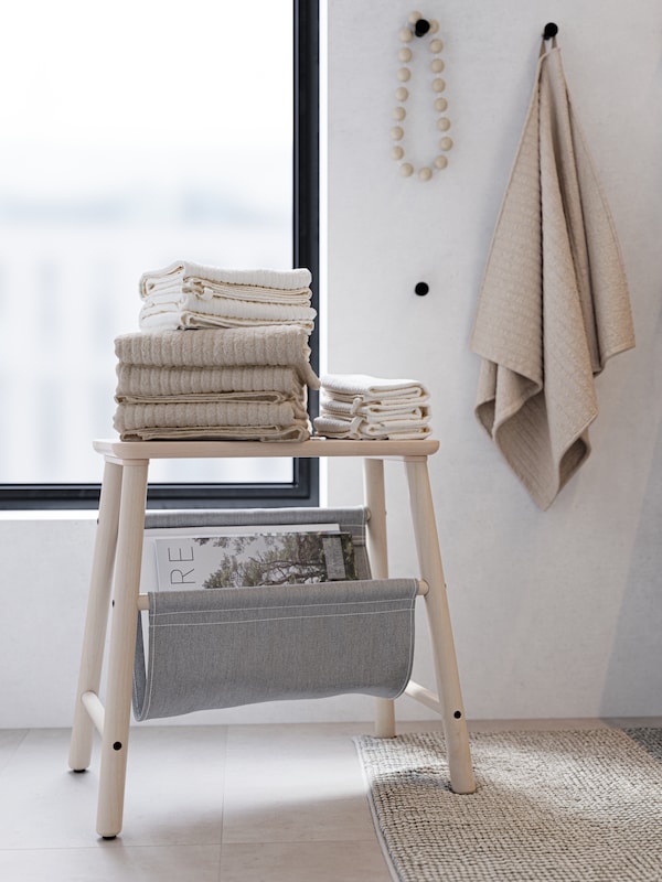 一个木制的凳子上,叠得整整齐齐的米色和白色的毛巾上。黑色钩子用米色的毛巾和木制项链。