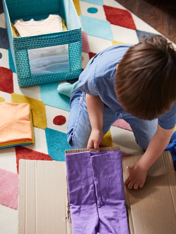孩子折叠衣服的协助下一块纸板,使他们在绿松石UPPRYMD盒丑角/多色地毯。