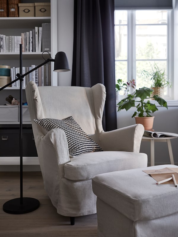 STRANDMON扶手椅和脚凳白色封面,前面的一个窗口和一个书架,一个黑色的落地灯。
