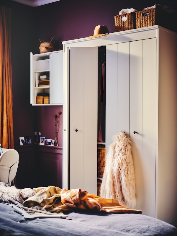 白色IDANAS衣柜有一个开放的折叠门和一件夹克挂在床附近的一个旋钮靠墙站。