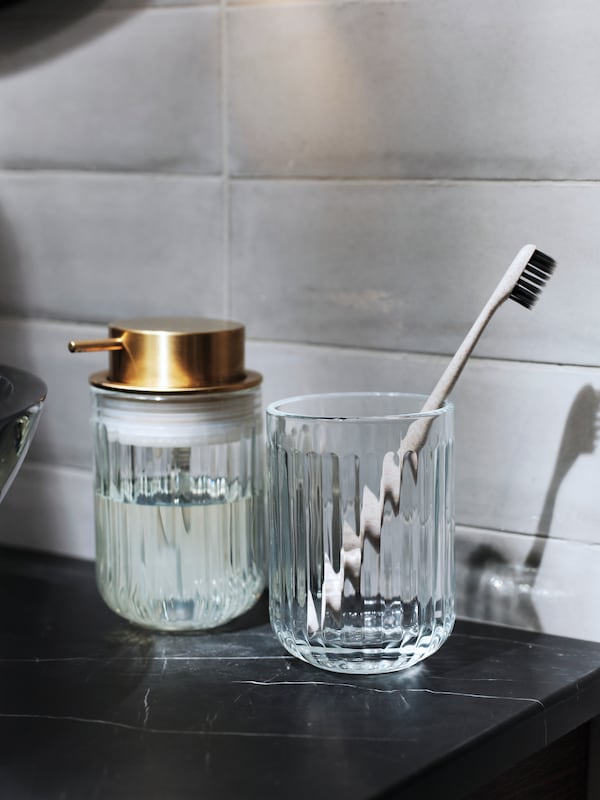 Badzubehör: Ein SILVTJÄRN Seifenspender und Ein Zahnbürstenhalter aus Glas stehen auf einer Oberfläche in Marmornachbildung。