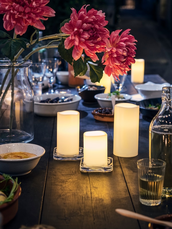 昏暗的表在户外被ADELLOVTRAD块蜡烛,照亮两侧有一个玻璃花瓶,花朵和餐具。