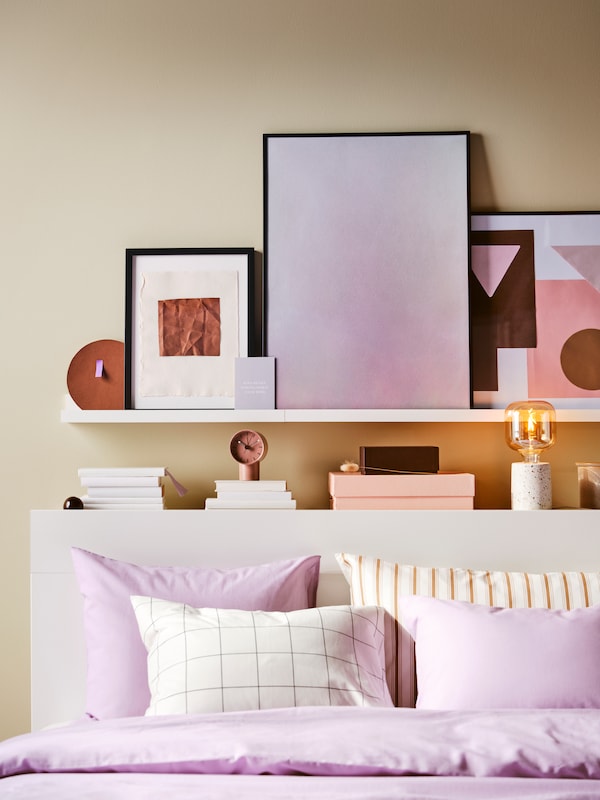 白色MOSSLANDA岩架与陷害艺术照片白色BRIMNES床头板的床上淡紫色NATTSVARMARE床单。