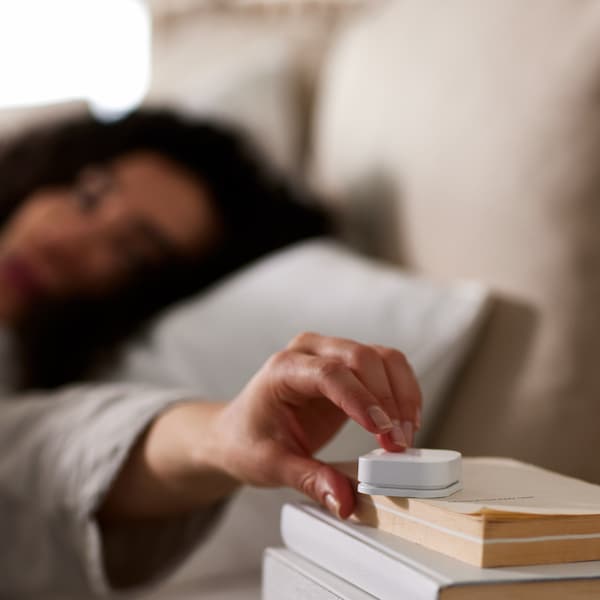 一个人躺在床上,伸出一只手按TRADFRI无线调光器坐在一堆书。