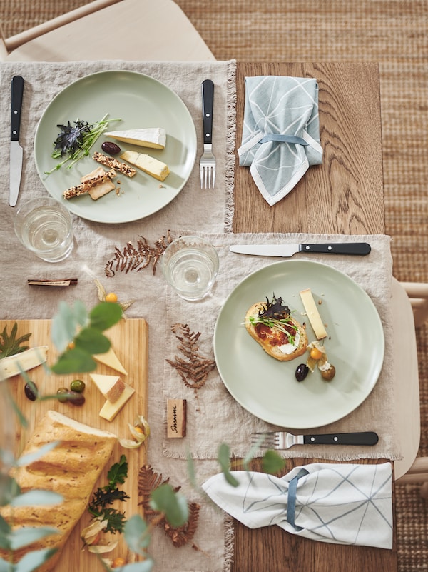 与餐巾纸装饰表的一个角落,黑色LIVNARA餐具,节日食品上马特绿色FARGKLAR盘子。
